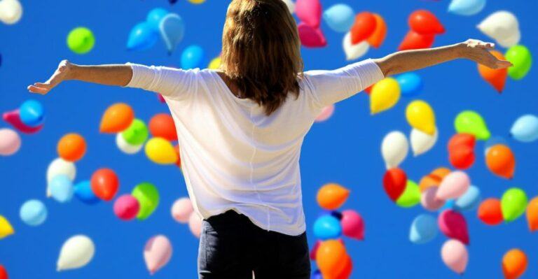 Kuvituskuvassa nainen seisoo selin kädet levällään kohti ilmassa lentäviä ilmapalloja